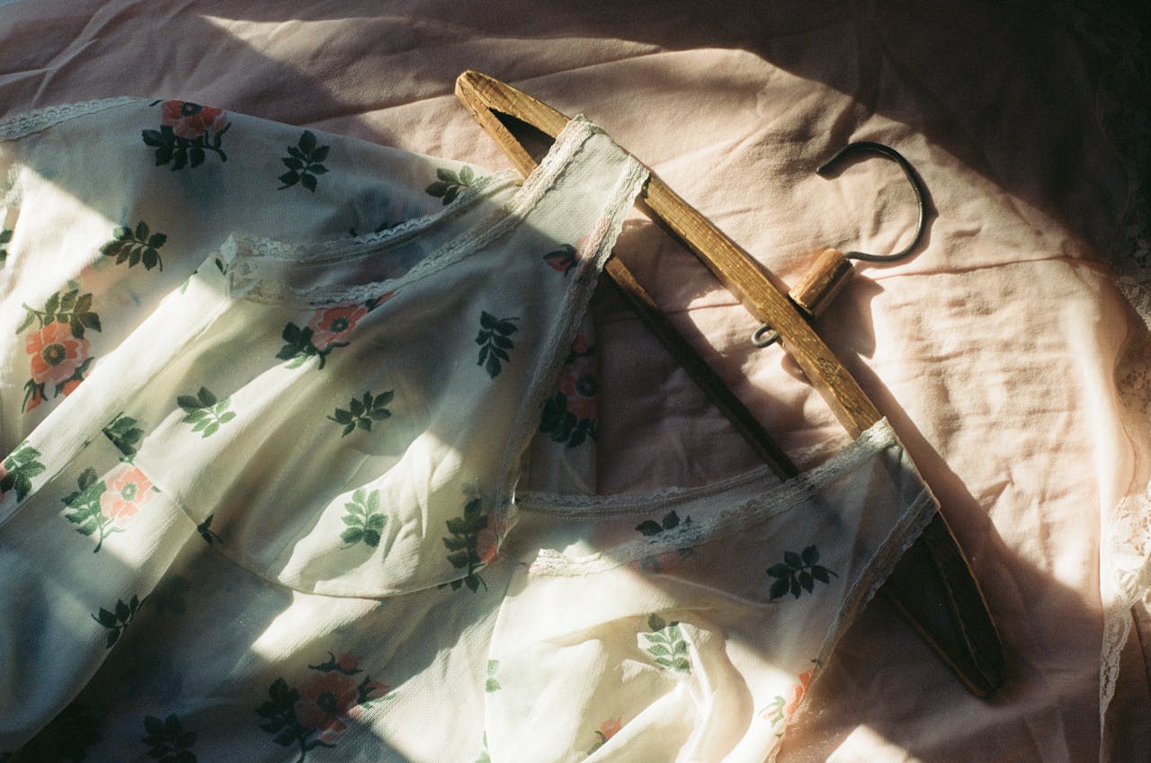 gallery-04 A floral dress with vintage flair elegantly draped on a wooden hanger, bathed in soft shadow play.